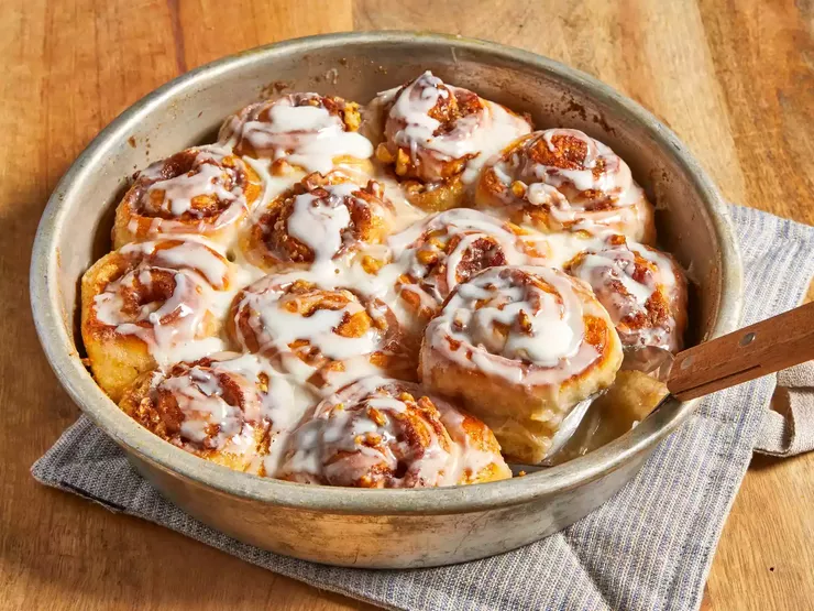 close up view of Cinnamon Rolls with icing in a round baking dish with a spatula